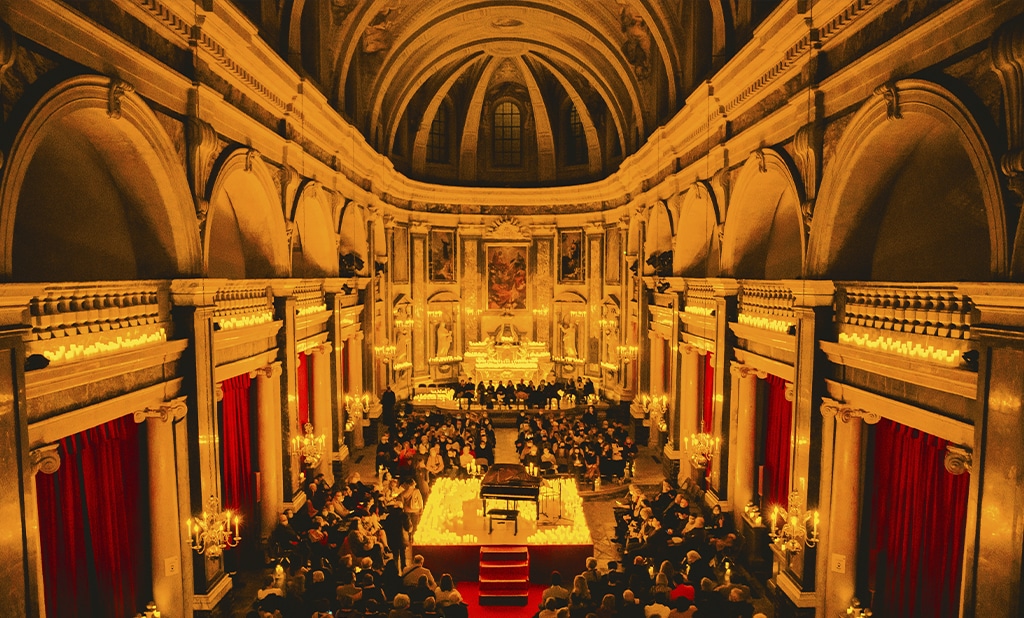Un piano est posé sur une estrade au centre d'une pièce, entouré de dizaines de bougies. Un public l'entoure, et regarde en direction du piano. C'est à l'intérieur de la Chapelle de la Trinité à Lyon.