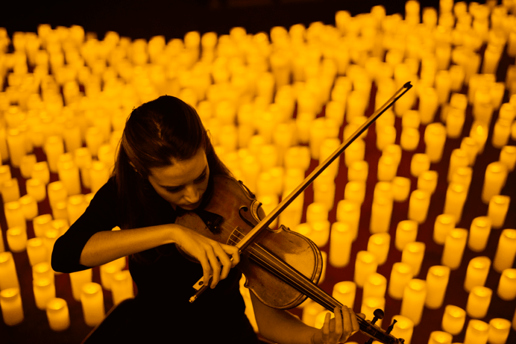 Concert Candlelight Une femme de face joue du violon entourée de milliers de bougies joue des musiques de films
