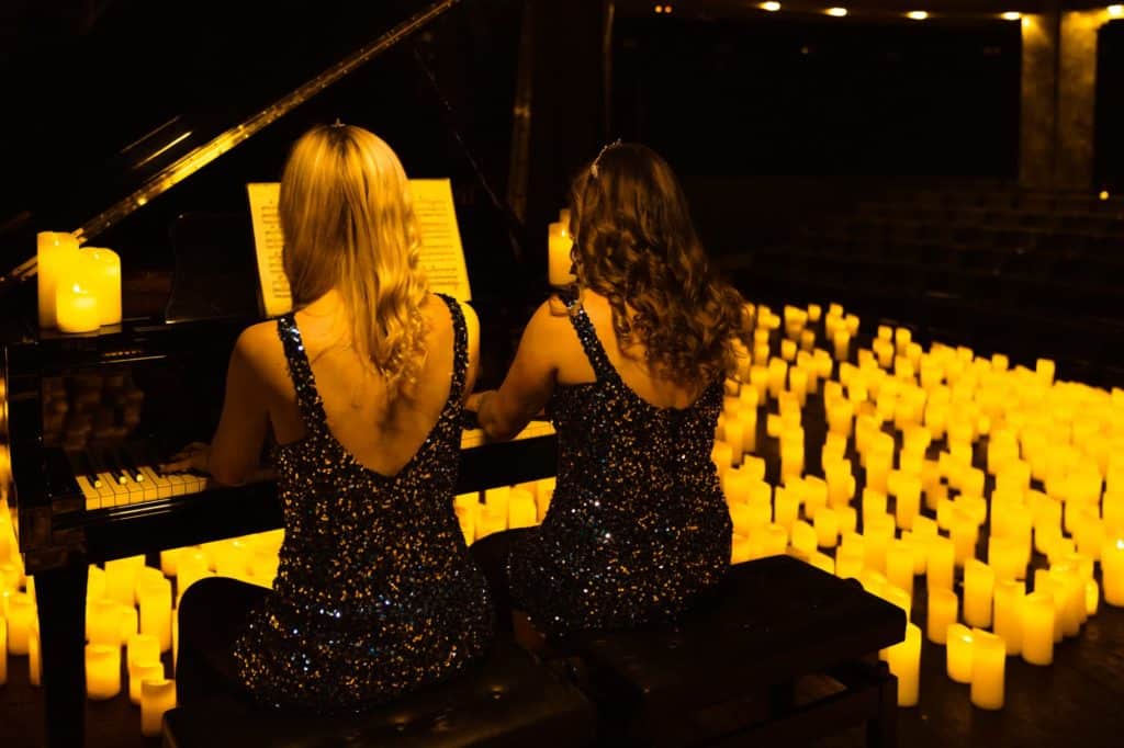 Concert Candlelight deux femmes de dos jouent au piano en duo entourées de milliers de bougies.