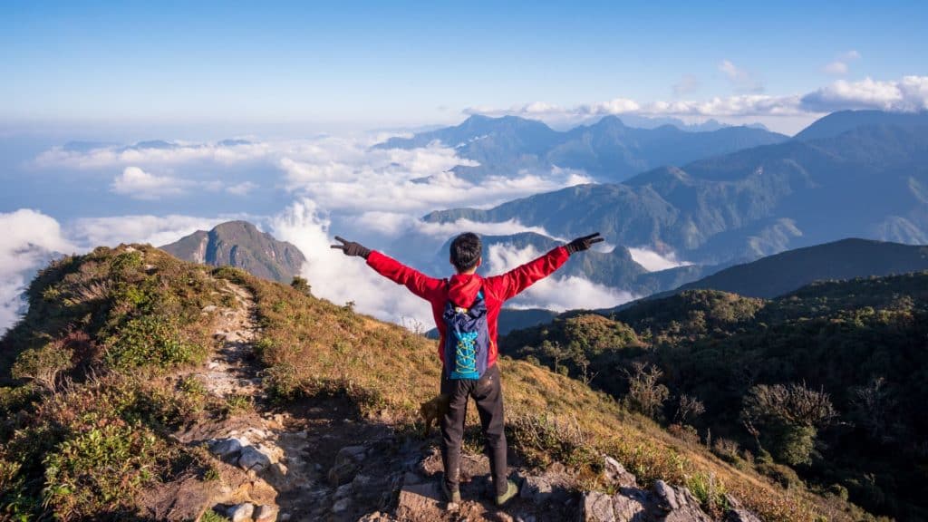 Photo d'un homme levant les bras de dos face à une montagne