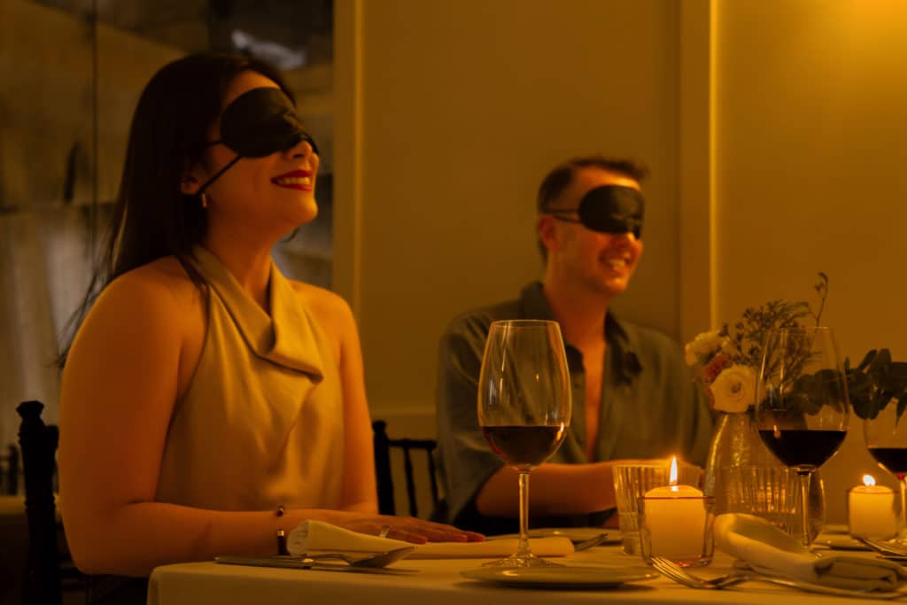 Un homme et une femme sont assis à table les yeux bandés avec un verre de vin pendant un repas à l'aveugle Dining in the Dark