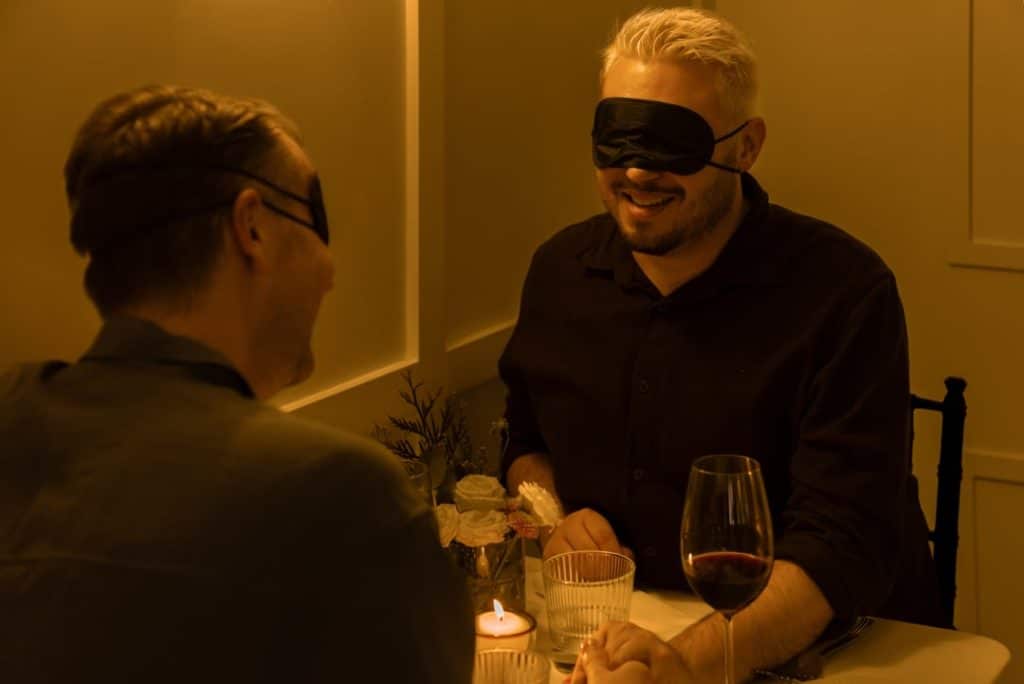 Deux hommes les yeux bandés partagent un repas à l'aveugle Dining in the Dark autour d'un verre de vin