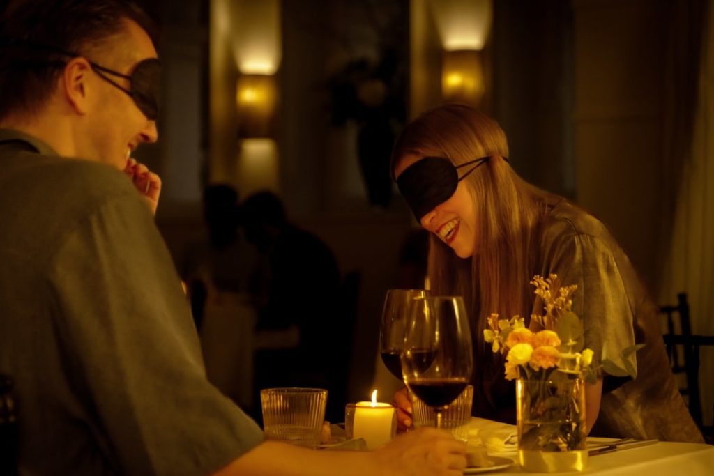 Un homme et une femme partagent un rire autour d'un repas à l'aveugle Dining in the Dark les yeux bandés