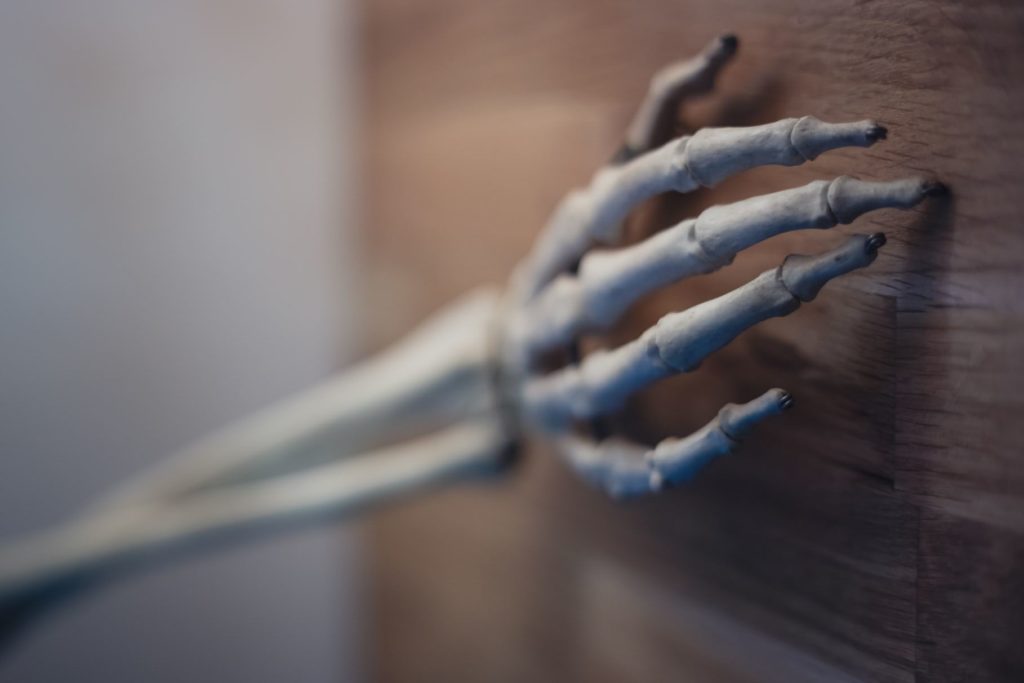 Photo d'un bras et d'une main de squelette posés sur une porte en bois